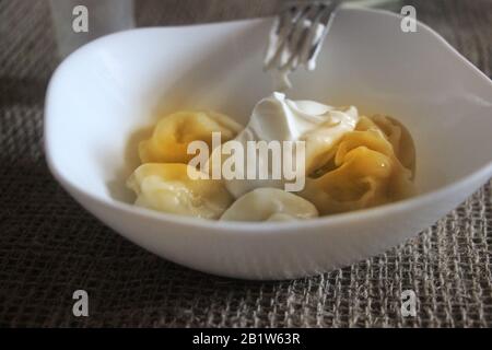 Fleischklöße - russisches Pelmeni mit saurer Sahne in weißer Schüssel auf einem Sacktuch stehend Stockfoto