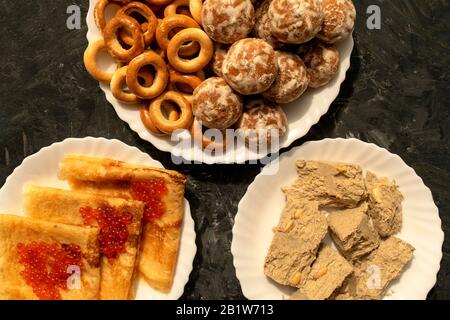 Frische Pfannkuchen mit rotem Kaviar, Sonnenblumen Halva, russischen Bagels und Lebkuchen auf grauem Hintergrund. Sortiment berühmter russischer Süßigkeiten. Stockfoto