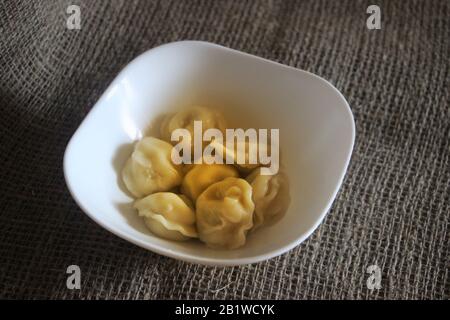 Fleischklöße mit Butter - russischer Pelmeni in weißer Schüssel auf einem Sacktuch stehend Stockfoto