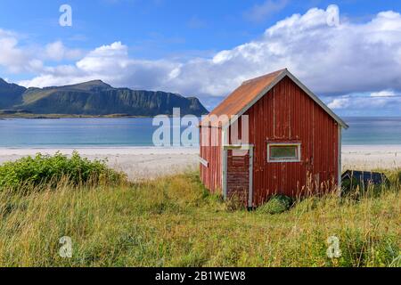 Sonniger Strand von Ramberg (Lofoten Island, Norwegen) mit roter Holzhütte Stockfoto