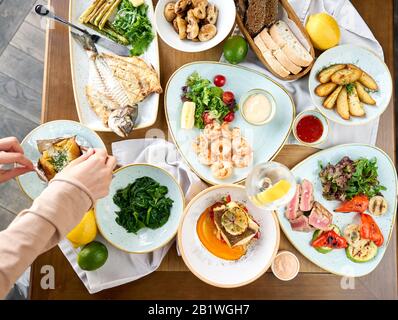 Viele verschiedene köstliche Gerichte auf dem Tisch. Verschiedene Snacks und Antipasti auf dem Tisch. Teller Fisch und Meeresfrüchte Grill mit Garnierung. Verschiedene Gerichte auf Stockfoto