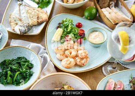 Viele verschiedene köstliche Gerichte auf dem Tisch. Verschiedene Snacks und Antipasti auf dem Tisch. Teller Fisch und Meeresfrüchte Grill mit Garnierung. Verschiedene Gerichte auf Stockfoto