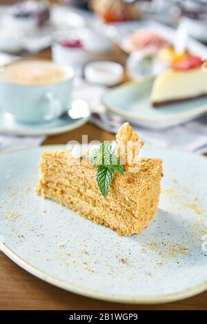 Honig Kuchen mit Baiser und Minze dekoriert.. Frühstück im Café, Kaffee am Morgen. Cappuccino und viele Desserts auf dem Tisch. Stockfoto