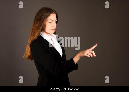 Attraktive junge Geschäftsfrau drückt virtuelle Taste über grauem Hintergrund Stockfoto