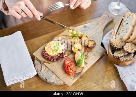 Mittagessen im Restaurant, eine Frau isst gebratenen Tintenfisch BBQ mit gebackenen Kartoffel. Holzplatte. Restaurant Menü Stockfoto