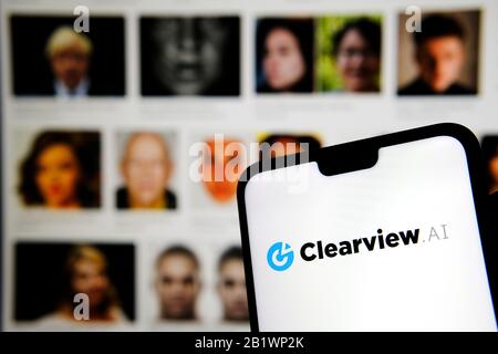 Das Firmenlogo von Clearview AI auf dem Smartphone-Bildschirm hält sich mit verschwommenen Gesichtern im Hintergrund in den Händen. Konzeptfoto für Gesichtserkennungssoftware. Stockfoto