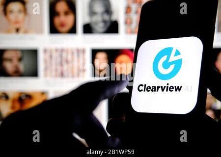 Das Firmenlogo von Clearview AI auf dem Smartphone-Bildschirm hält sich mit verschwommenen Gesichtern im Hintergrund in den Händen. Konzeptfoto für Gesichtserkennungssoftware. Stockfoto