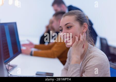 Junge Geschäftsfrau, die an ihrem Schreibtisch sitzt und lächelt. Glücklicher erfolgreicher Business Leader, der im Hintergrund arbeitet. Stockfoto