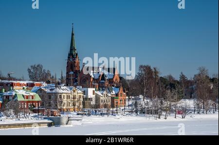 Umea City Kirche im Winter bewölkten Tag, Schweden. Gefrorener Umea Fluss im Vordergrund. Blauer Himmel, keine Wolken. Vasterbotten County, Schweden. Stockfoto