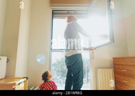 Baby beobachtet seine Mutter beim Reinigen und Tiden des Hauses. Stockfoto