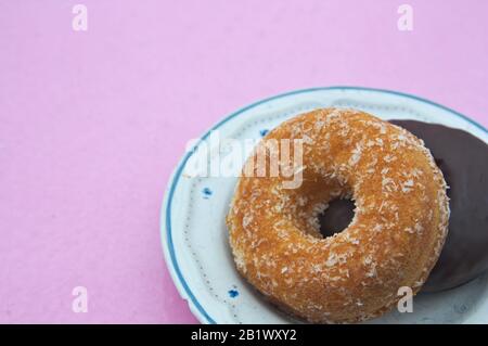 Zwei Donuts, eins mit Kokosnuss und eins mit Schokolade auf einem Teller und einem pinkfarbenen Hintergrund, um Texte hinzuzufügen (Kopierraum) Stockfoto