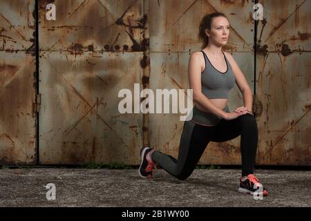 Schöne junge Frau Workout mit Ausfallschritt in rauer Tür in der städtischen Industrieumgebung Stockfoto