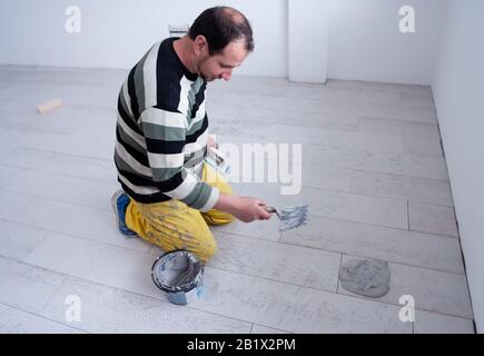 Verfugen von Keramikfliesen. Tiler füllen den Raum zwischen Keramikfliesen aus Holz mit einem Gummi-Trowel auf dem Boden in einer neuen modernen Wohnung Stockfoto