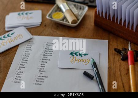 Hochzeitskalligraphie - Gästeliste und handschriftliche Platzkarten mit Namen. Goldenes Schreiben mit grünem Papier blüht auf. Stockfoto