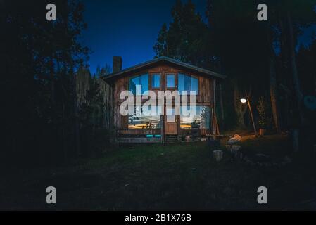 Bariloche, ARGENTINIEN, 19. JUNI 2019: Außenansicht einer gemütlichen und entspannenden Holzhütte im Wald in den letzten Lichtmomenten mit Sonnenuntergang Stockfoto