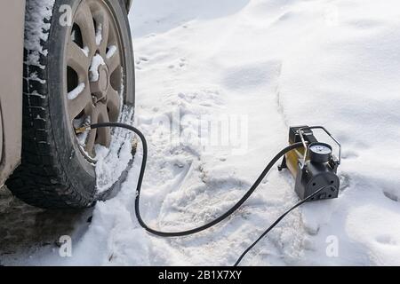 Pumpe, Autokompressor zum Aufpumpen von Reifen mit Luft steht im Winter auf dem Schnee und pumpt den flachen Reifen des Wagens Stockfoto