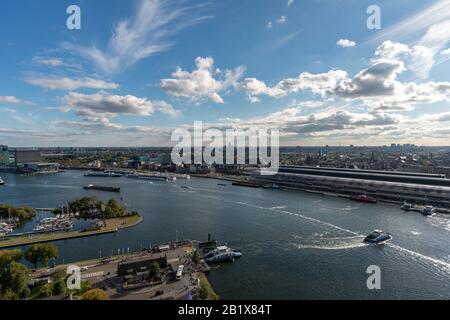 Der Hafen von Amsterdam mit dem Fährschiff, das über den IJ-Fluss führt, mit dem historischen Stadtzentrum und dem Hauptbahnhof im Hintergrund Stockfoto