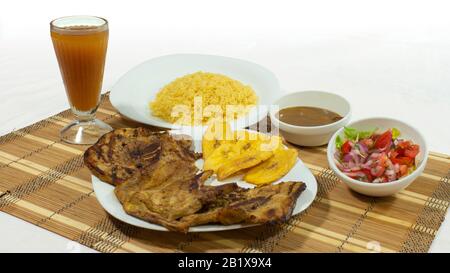 Weiße Platte mit Schweinekopf, begleitet von gebratener Banane, Salat und gelbem Reis mit einer Glaskasse mit Limonade auf weißem Hintergrund Stockfoto