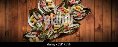 Blick auf Gerichte mit Fisch Maitos, typische Gerichte des ecuadorianischen Amazonas, begleitet von Maniok, gekochten Bananen und Salat auf einem Holztisch Stockfoto