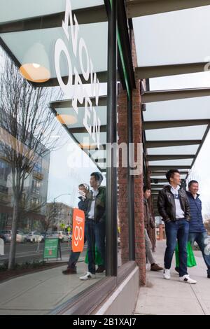 Ein Kunde überquert die Pike Street, nachdem er am 27. Februar 2020 bei Amazon Go Grocery einkauft. Der erste große, kashierlose Supermarkt des Technikunternehmens wurde Anfang der Woche im Viertel Capitol Hill in Seattle eröffnet. Kunden scannen eine Amazon Go App, um in den 10.000 Quadratfuß großen Laden zu gehen, die Produkte zu nehmen und ohne Auschecken zu gehen. Die "Just Walk Out Technology" von Amazon nutzt ein komplexes System von Kameras und Sensoren, um Einkäufe nachzuverfolgen, das bereits in ihren kleineren Amazon Go Convenience Stores verwendet wird. Stockfoto