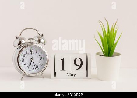 19. Mai auf einem Holzkalender neben einem Wecker und einer Blume. Ein Tag des Frühlingsmonats, Kalender und Wecker auf hellem Hintergrund. Frühling i Stockfoto