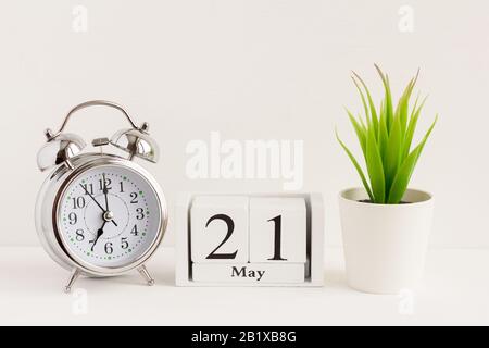 21. Mai auf einem Holzkalender neben einem Wecker und einer Blume. Ein Tag des Frühlingsmonats, Kalender und Wecker auf hellem Hintergrund. Frühling i Stockfoto