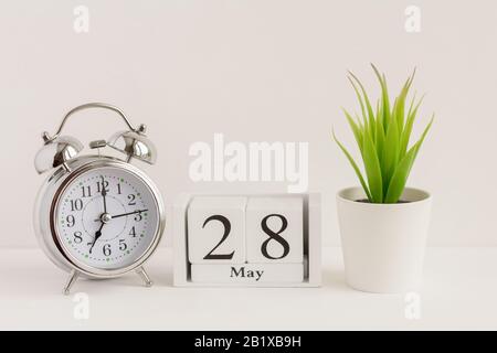 28. Mai auf einem Holzkalender neben einem Wecker und einer Blume. Ein Tag des Frühlingsmonats, Kalender und Wecker auf hellem Hintergrund. Frühling i Stockfoto