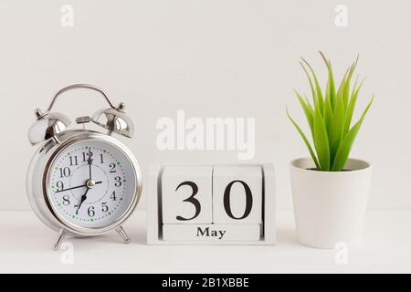 30. Mai auf einem Holzkalender neben einem Wecker und einer Blume. Ein Tag des Frühlingsmonats, Kalender und Wecker auf hellem Hintergrund. Frühling i Stockfoto