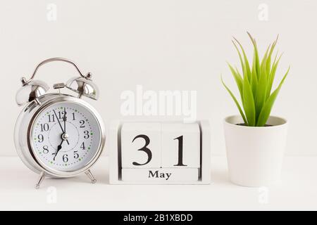Mai auf einem Holzkalender neben einem Wecker und einer Blume. Ein Tag des Frühlingsmonats, Kalender und Wecker auf hellem Hintergrund. Frühling i Stockfoto
