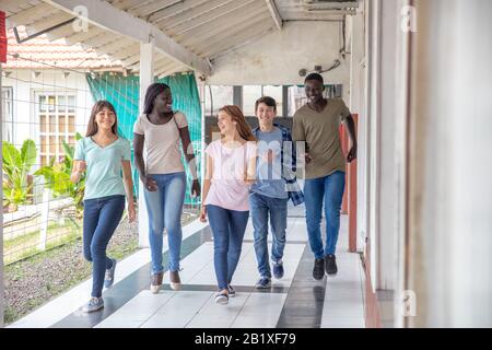 Gruppe gemischter Rennen Teenager, die im Schulflur spazieren und lächeln. Stockfoto