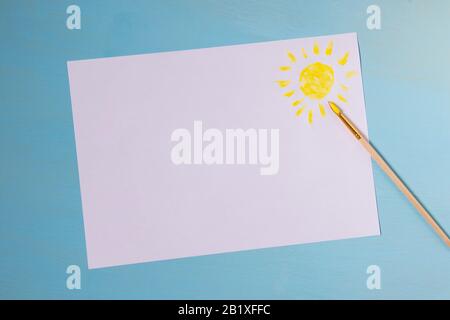 Copyspace auf weißem Blatt Papier mit blauem Hintergrund ein Ort für die Beschriftung und mit gelber Sonne und Pinsel bemalt Stockfoto