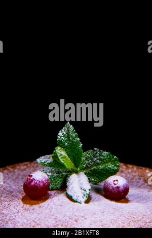 Preiselbeeren liegen auf gebackenem Pfannkuchen mit grüner Minze, die mit Puderzucker bestreut ist, auf einem schwarzen Hintergrund, vertikaler Fotoansicht Stockfoto