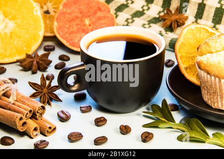 Ein Becher schwarzen Kaffees auf einem blauen Tisch mit einer kupchengrünen Serviette und Zimt verstreuten Kaffeebohnen und in Scheiben geschnittenen orangefarbenen Scheiben Stockfoto