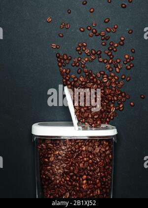Gebratene Kaffeebohnen sind auf grauem Hintergrund aus dem Mixbecher verschüttet worden Stockfoto