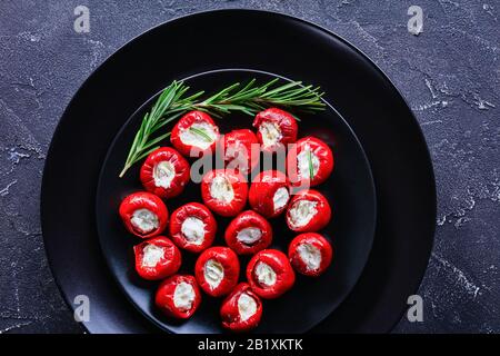 Ricotta-Käse gefüllte heiße Kirschpfeffer auf einem schwarzen Teller mit Rosmarinsprigen auf dunklem Betongrund, horizontale Ausrichtung, Nahaufnahme Stockfoto