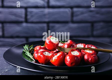Kirschpfeffer mit weichem Ricotta-Käse serviert auf einem schwarzen Teller mit Rosmarinsprig auf dunklem Betongrund vor einer schwarzen Ziegelwa Stockfoto