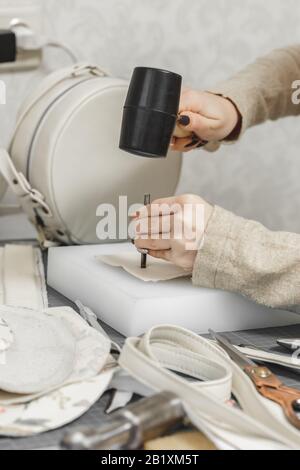 Nahaufnahme der Hände der Frau, die mit einem Hammer mit Naturleder arbeiten. Handtaschenmeister bei der Arbeit in der örtlichen Werkstatt. Weibliches Besetzungskonzept Stockfoto