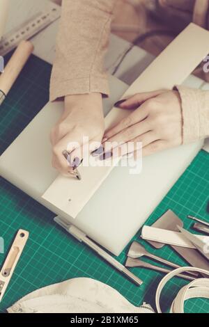 Nahaufnahme der Hände der Frau, die mit einem Hammer mit Naturleder arbeiten. Handtaschenmeister bei der Arbeit in der örtlichen Werkstatt. Weibliches Besetzungskonzept Stockfoto