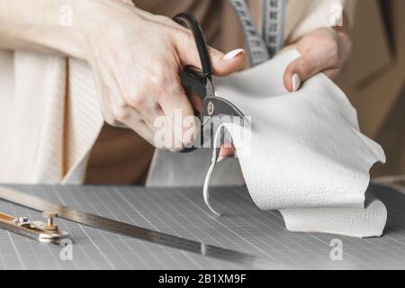 Damenhandtaschendesignerin misst Leder und schneidet Details in einem Werkstatt-Studio aus Stockfoto