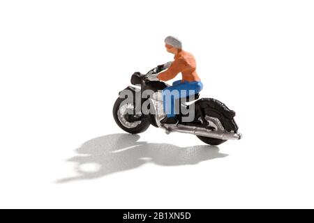 Miniatur-Person, die mit einem Motorrad mit Schatten über einem weißen Hintergrund in Seitenansicht und Kopierbereich unterwegs ist Stockfoto