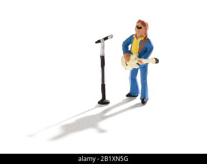 Miniaturgitarrist und Sänger stehen vor einem mike, der während eines Live-Auftritts auf Weiß mit Schatten singt Stockfoto