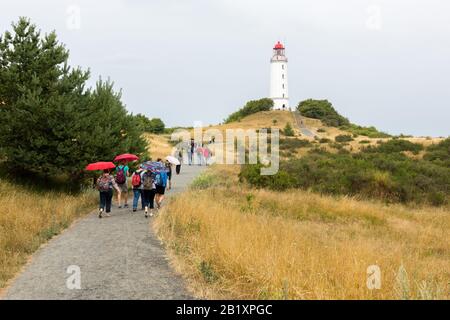 Historischer Dornbuscher Leuchtturm auf der Insel Hiddensee (ostsee) an einem regnerischen Tag. Touristen mit Sonnenschirmen, die zum Leuchtturm laufen. Stockfoto