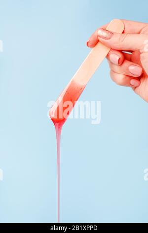 Enthaarung und Schönheitskonzept - Zuckerpaste oder Wachshonig zur Haarentfernung mit Holzwachspachtelstäbchen in der Hand auf blauem Hintergrund, Kopierraum, B. Stockfoto