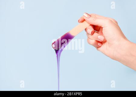 Enthaarung und Schönheitskonzept - Zuckerpaste oder Wachshonig zur Haarentfernung mit Holzwachspachtelstäbchen in der Hand auf blauem Hintergrund, Kopierraum, B. Stockfoto