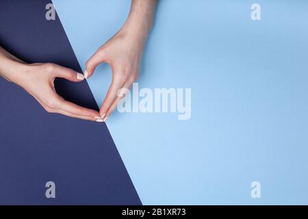 Weibliche Hände zeigen ein Herzsymbol auf blauem geometrischem Hintergrund. Platz für Text. Stockfoto