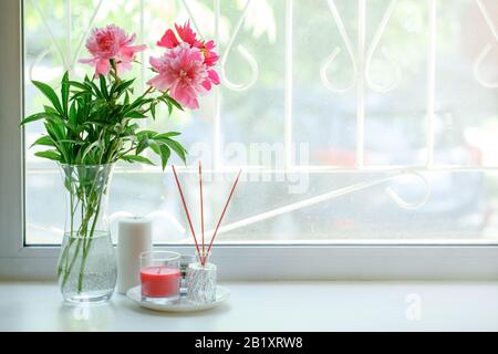 Vase mit Blumen auf der Fensterbank. Kerzen und Blumenstrauß mit pinkfarbenen Ponys. März, Frauentag. Muttertag. Wunderschöner romantischer Morgen. Selektiv Stockfoto