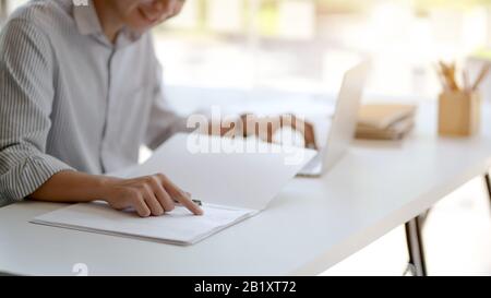 Zugeschnittenes Foto von männlichen Unternehmern, das sich auf seine Dokumentdatei auf weißem Tisch in Glaswandbüro konzentriert Stockfoto