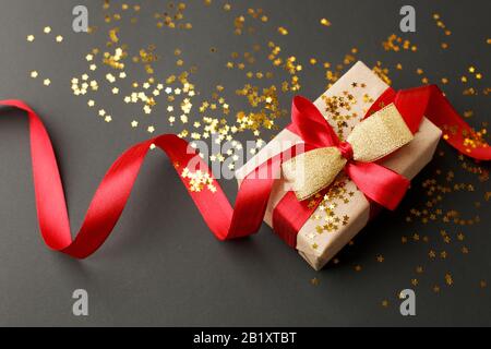 Geschenkschachtel mit Kunsthandwerk auf dunklem Hintergrund, mit strukturierter Schleife und Federn dekoriert, was eine romantische Luxusatmosphäre schafft. Zum Geburtstag, zum Jubiläum Stockfoto