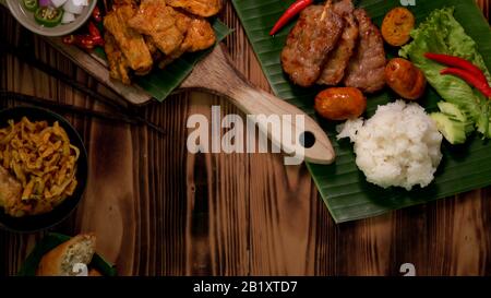 Blick auf thailändische traditionelle Straßengerichte mit gegrilltem Schweinefleisch, Schweinesatay, klebrigem Reis, Khao Soi und Kopierraum auf rustikalem Tisch Stockfoto