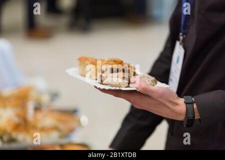Nahaufnahme von Mann mit Halteplatte und schaufeldem Essen am Tisch in Buffetform, Catering im Hotel oder Restaurant, Business Conference. Stockfoto